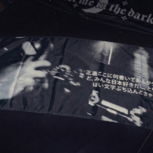 Flaga Nobori "Japońskie pie*dolenie" w stylu JDM, czarno-biała, rozłożona na masce ciemnego samochodu w garażu, z widocznym japońskim tekstem.